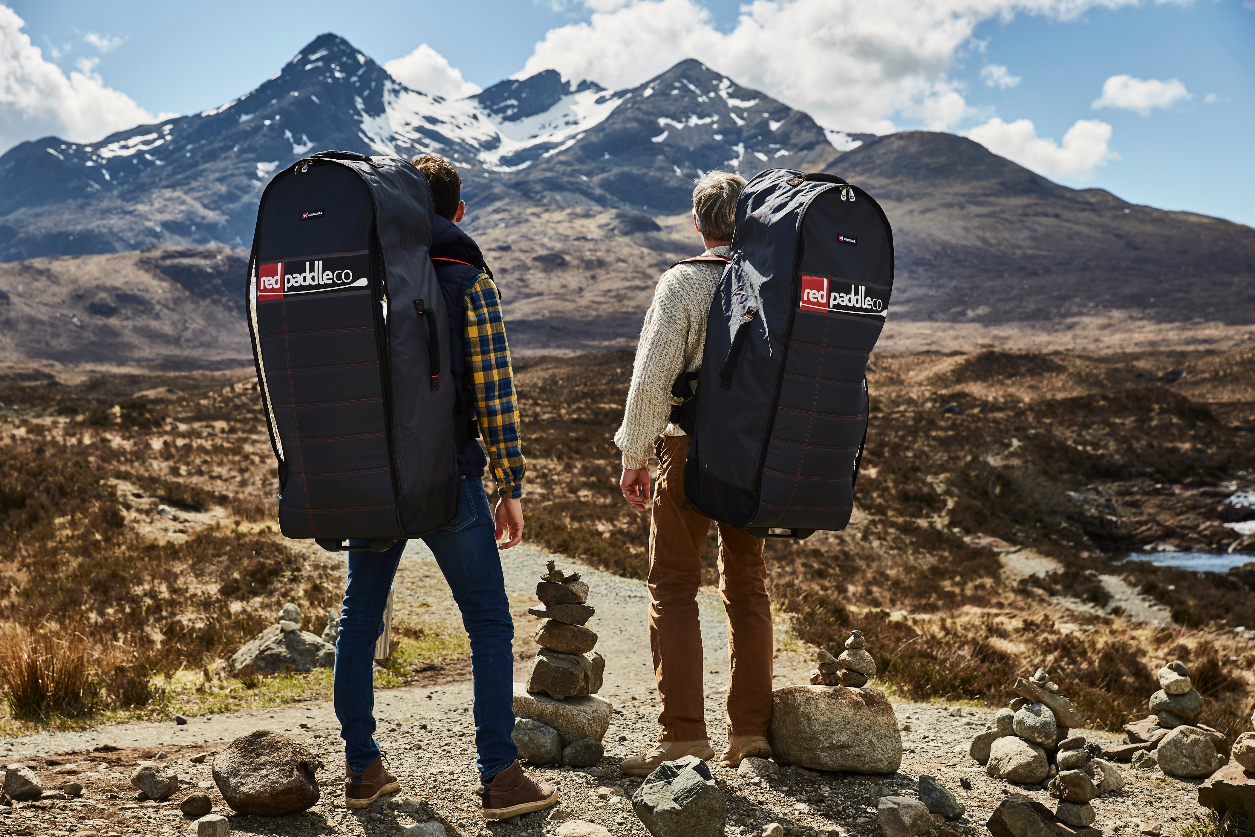 two men with red paddle co all terrain backpacks on the isle of skye, two paddle boarders on a Scottish loch at sunset, laughing woman helping a lamb off an inflatable paddle board,