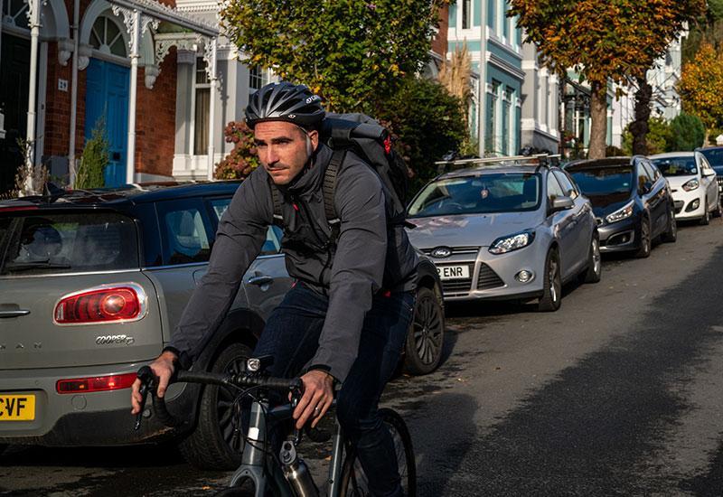 Man riding a bike down a street with cars parked at the side