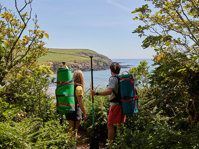 Man and woman carrying Red Original SUP’s whilst looking out to sea