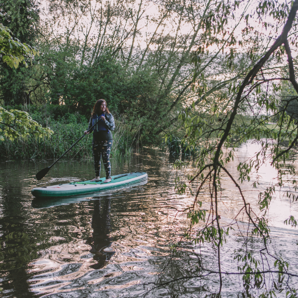 Natasha Sones stood on Red Paddle Co 12'6" Voyager inflatable paddleboard on a lake amongst some trees