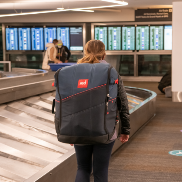 Woman carrying Red Paddle Co 12'0" Compact MSL PACT through airport baggage claim.