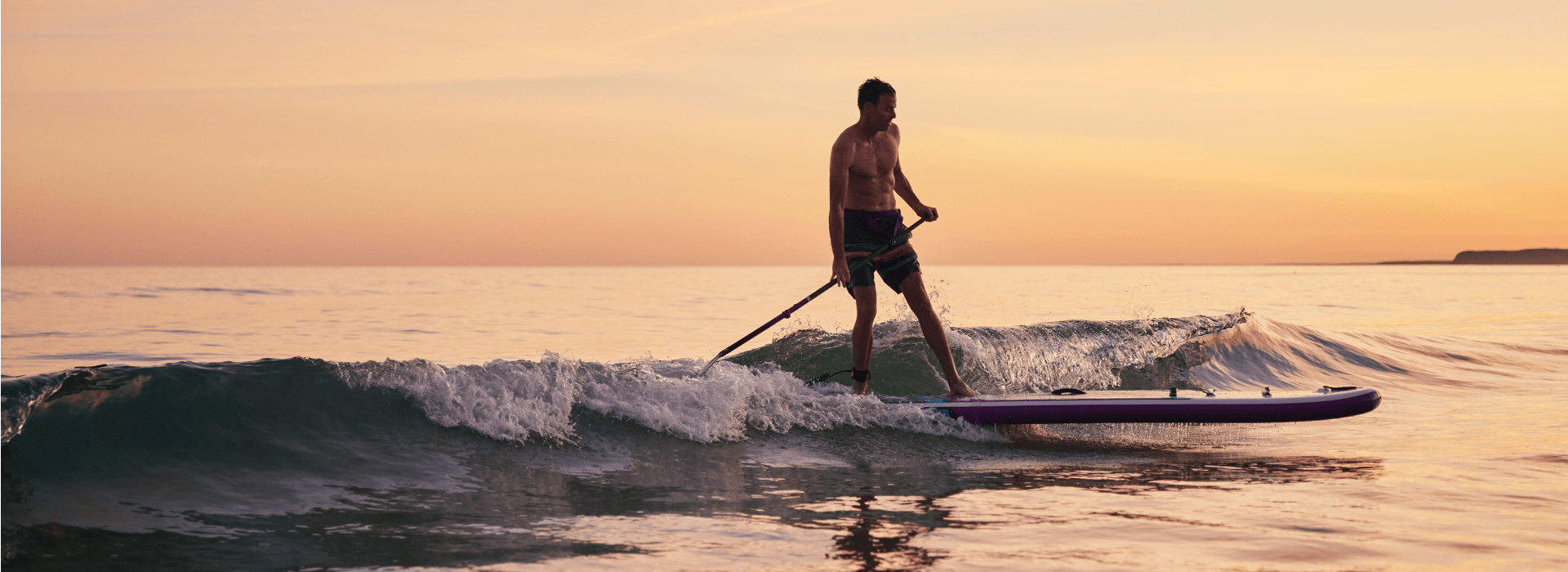 A man paddleboarding in the sea at sunset