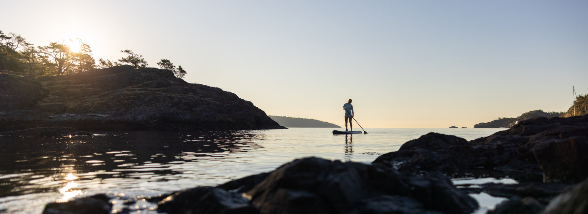 A person paddleboarding into the ocean during sunset