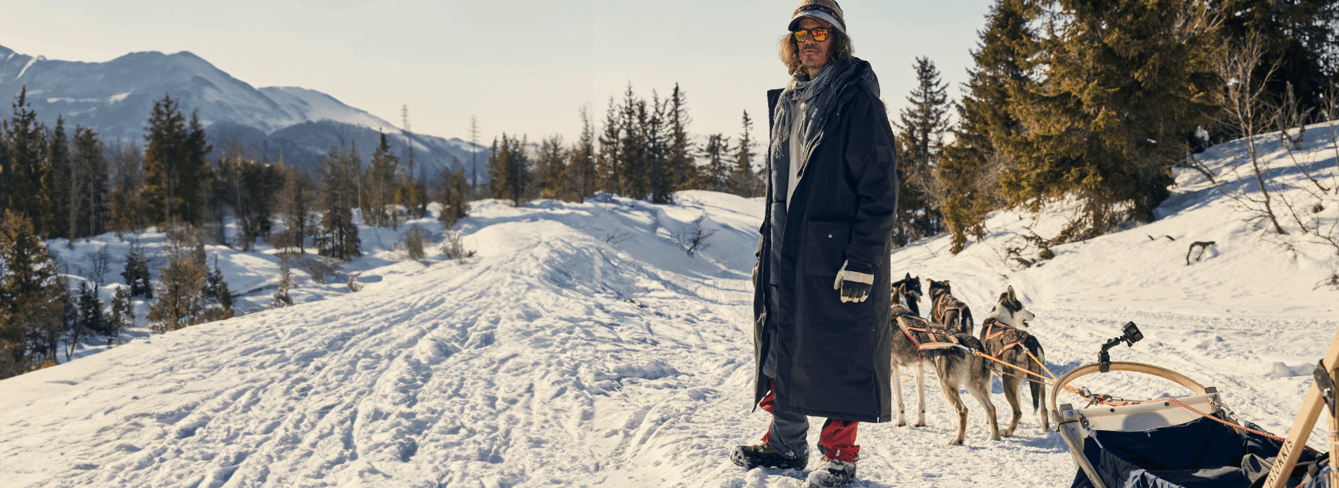 A man hiking in the snow with his dogs pulling a sled