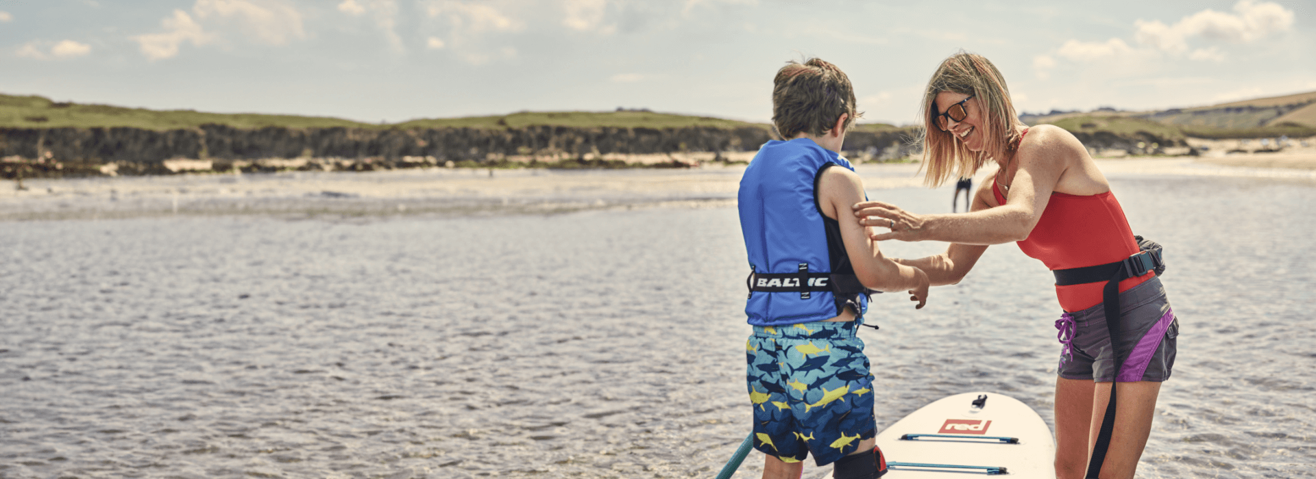 A woman helping her son to put on his lifejacket before going on the paddleboard