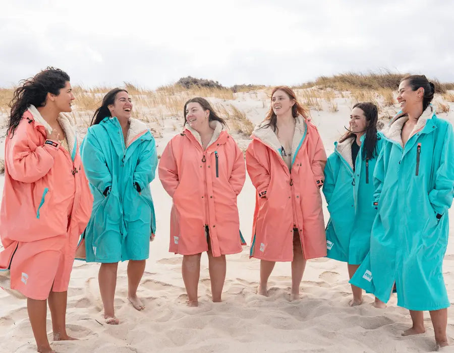 A group of women smiling and laughing on the beach wearing the new long sleeve pro change robes