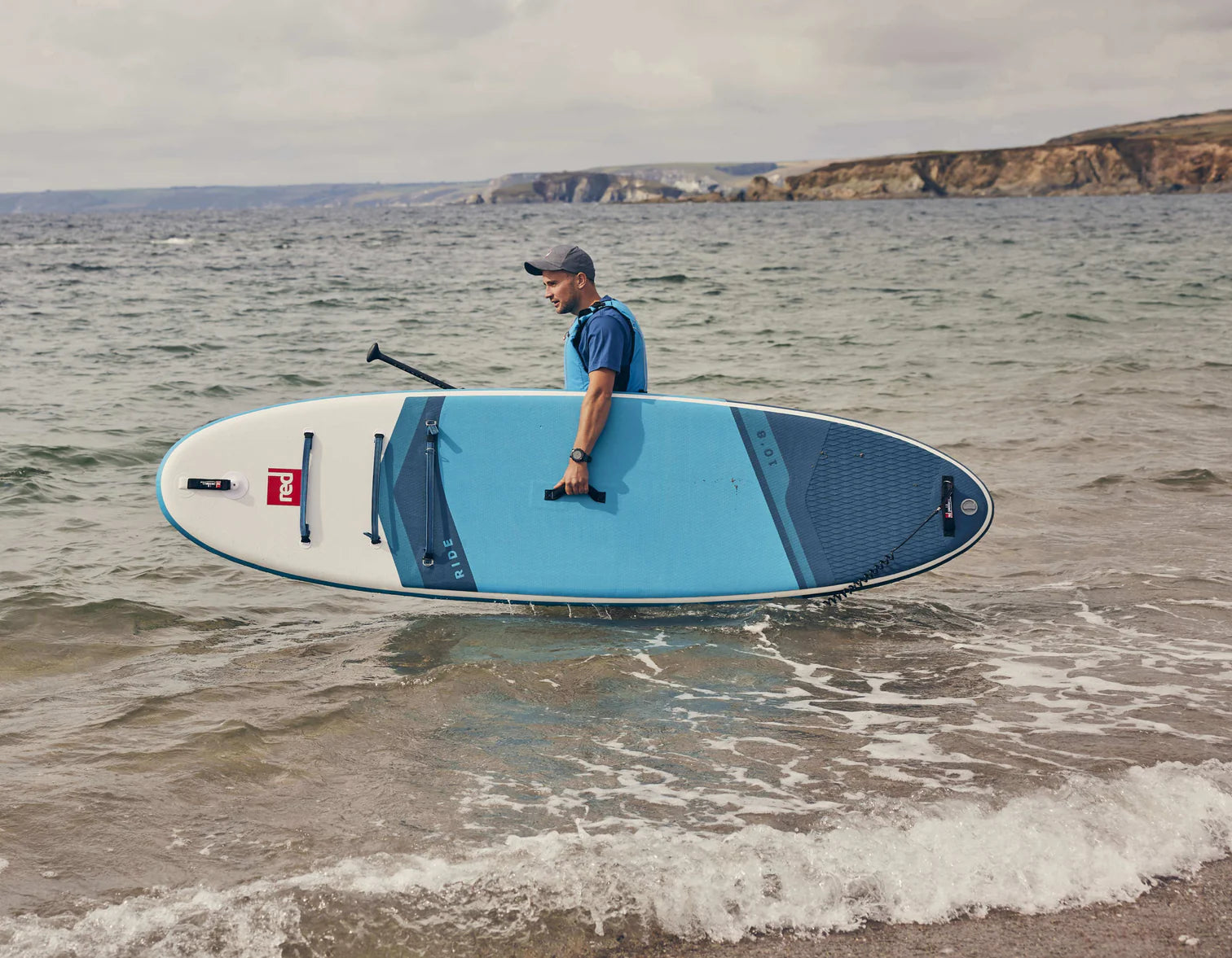 A man walking into the sea carrying his Red paddleboard