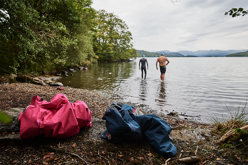 Two men walking into a lake to swim