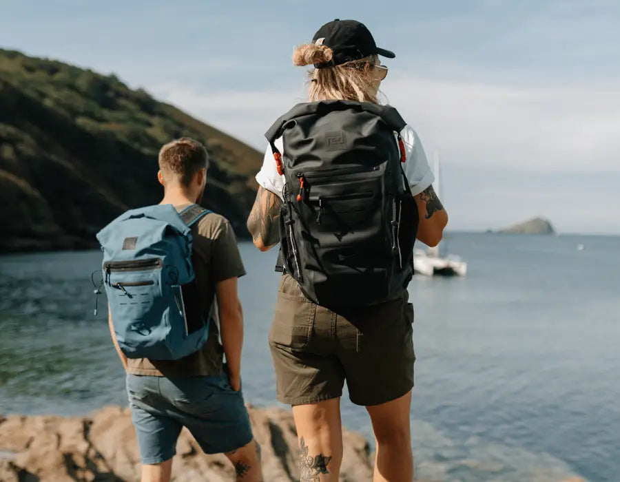 2 people carrying the Red Adventure Back Bag looking out to sea