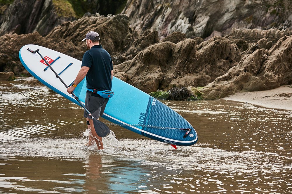 man wading into the sea carrying a paddle board