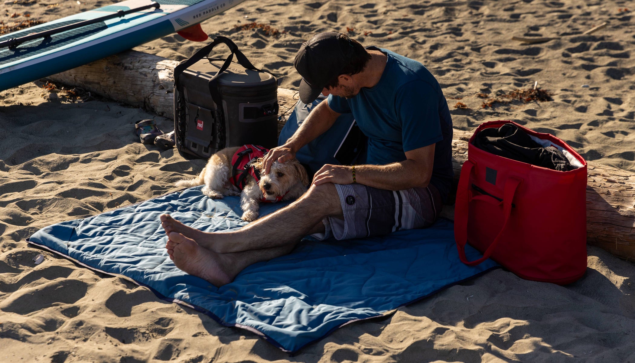 man sitting on red adventure outdoor blanket on the beach 