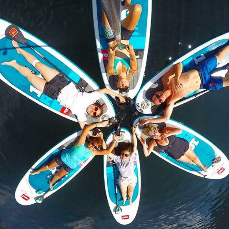 A group of paddleboarders all lying on their paddleboards in a circle