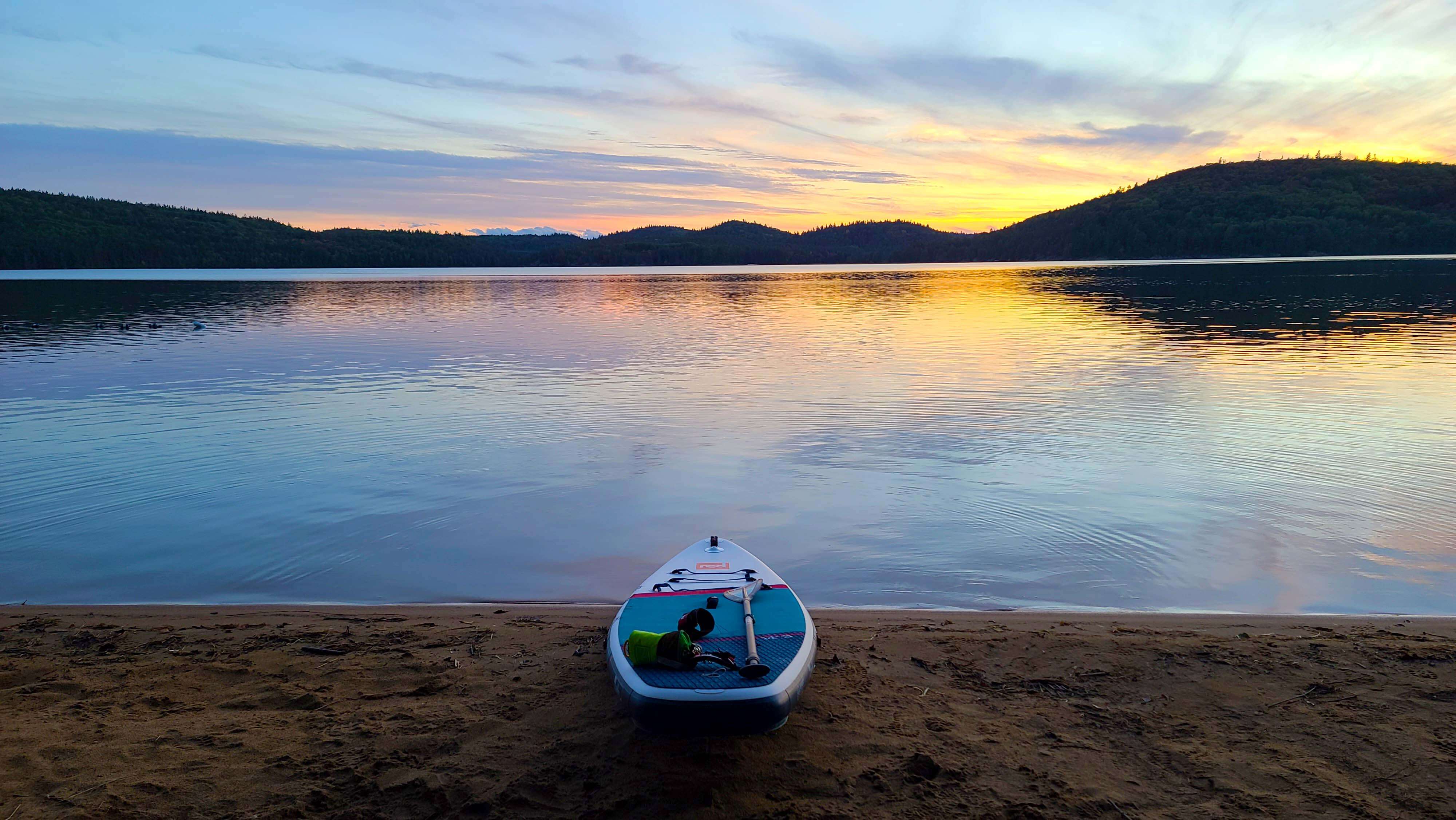 picturesque lake at sunset with Red inflatable paddle board on the shoreline