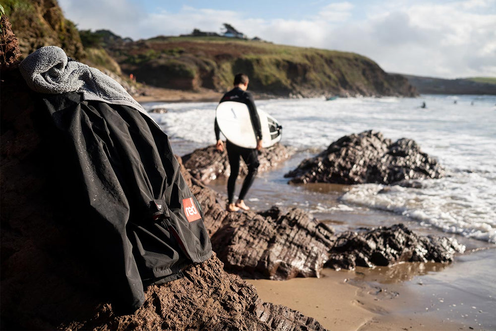 Man in a wetsuit holding a paddle board by the shore