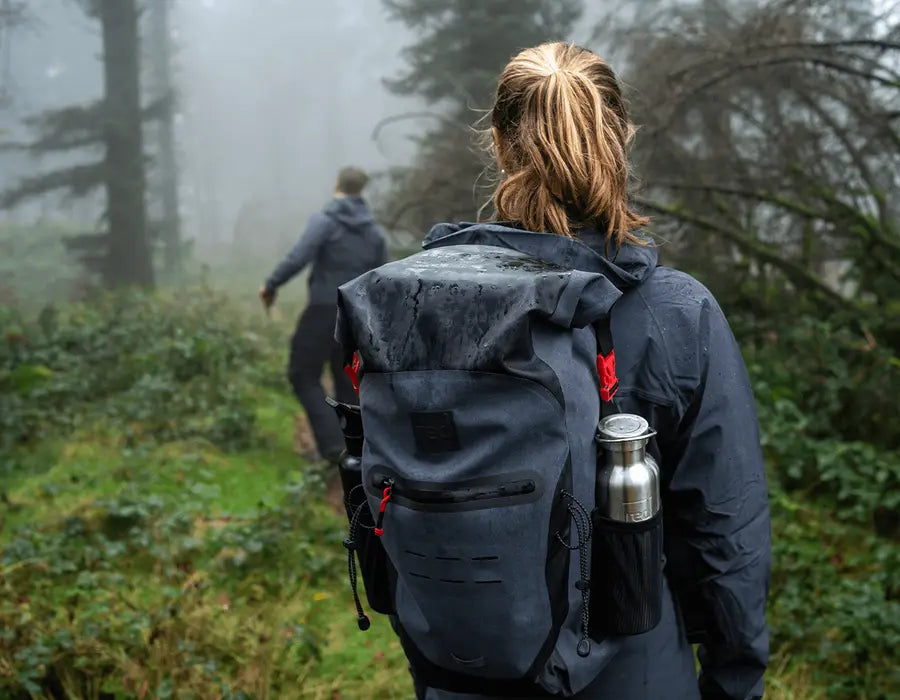 A woman wearing a waterproof backpack while walking in the forest in the rain