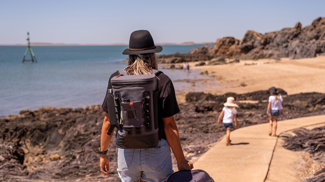 Woman walking on the beach with a grey cooler backpack