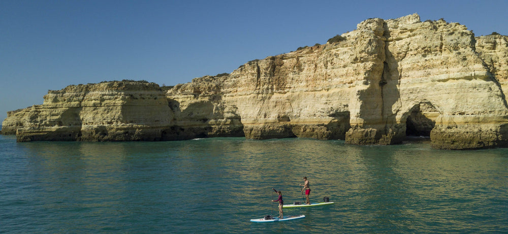 2 people paddle boarding in front of a cliff