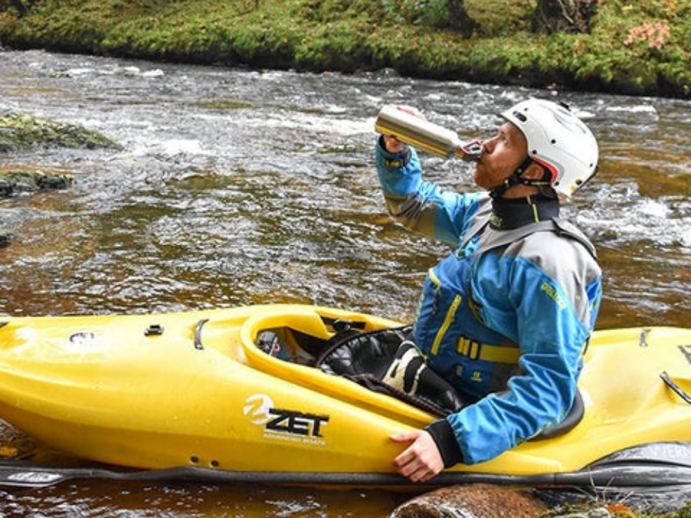 man drinking from red original water bottle on river