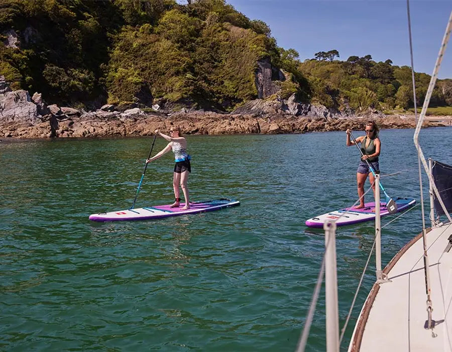 2 women paddleboarding next to a boat in the sea