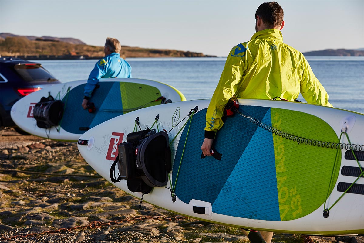 2 Men carrying Red Original Paddle Boards to a car on a beach