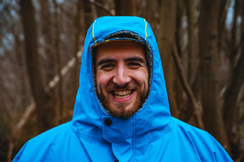 Man wearing Red Original Waterproof Changing Robe In Blue while in a wooded area