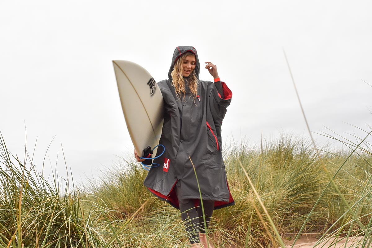 Woman in a Red Original Changing Robe Carrying A Surfboard