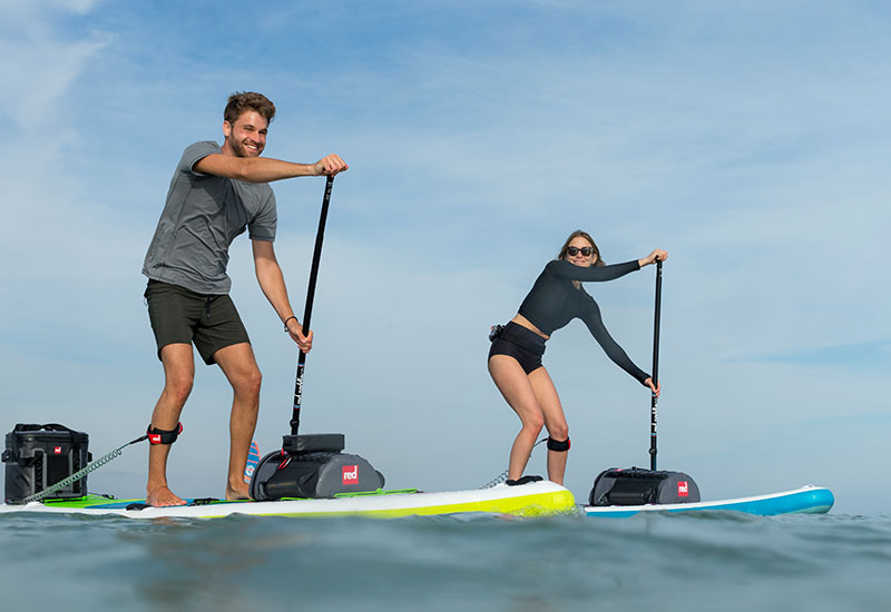 Man and Woman Paddle Boarding In the Sea With Deck bags attached to the front of their boards