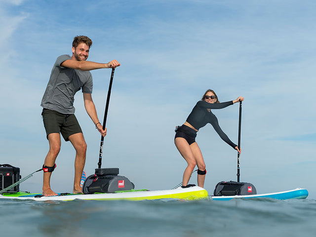 Man and Woman Paddle Boarding In the Sea With Deck bags attached to the front of their boards