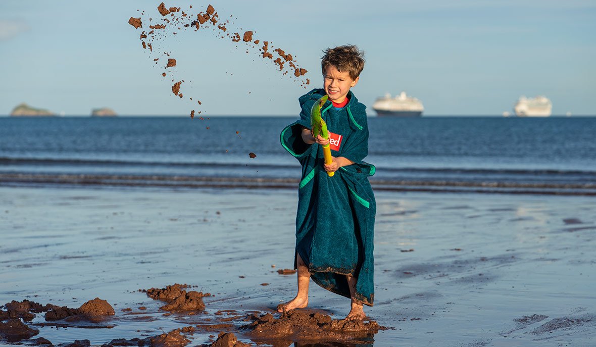 Family on the beach wearing change robes and towelling robes with Paddle Boards