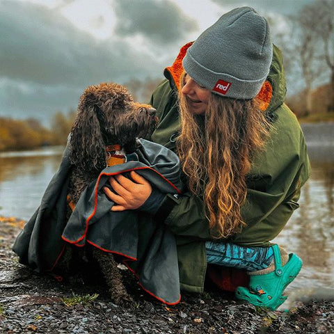 A woman wearing a Red Original Pro Change Robe EVO in Parker Green and Voyager Beanie in Graphite, drying her wet dog with a Large Microfibre Towel