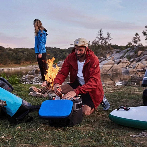 Man taking a bottle out of Red Original Cool Bag with a campfire in the background