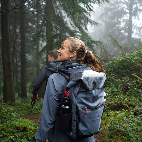 A man and a woman walking through the woods wearing Red Original Waterproof Active Jacket and carrying the Waterproof Backpack