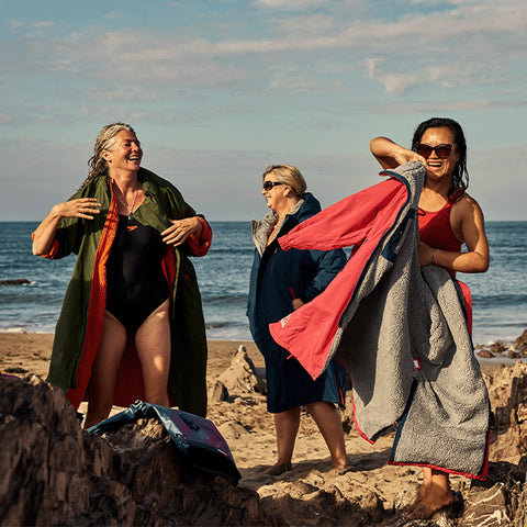 3 Women on a beach laughing and putting on their Pro Change Robe EVO after a swim in the sea