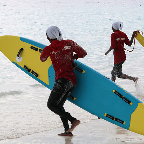 Two lifeguards at the water's edge running with a Red Rescue Inflatable Rescue Board
