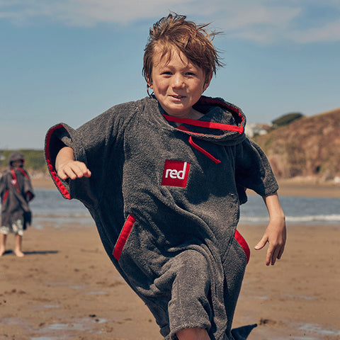 A boy running on the beach wearing the Red Original Kid's Towelling Change Robe in Grey