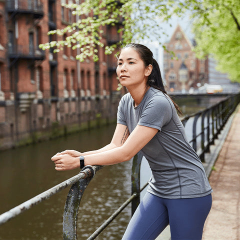 Woman leaning on a railing next to a canal in a city wearing workout gear including Red Original Women's Performance T-Shirt in Grey