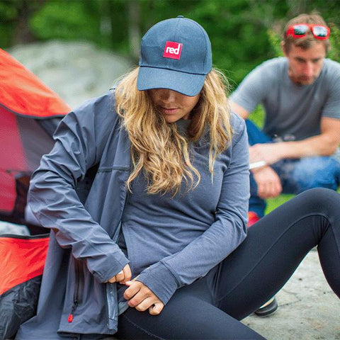 Woman wearing Red Original Paddle Cap, Waterproof Active Jacket and Performance Top Layer and a man wearing Performance T-Shirt in grey, sat outside a tent