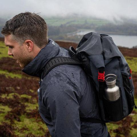 Man wearing Red Original Active Jacket, Waterproof Backpack with Stainless Steel Drinks Bottle whilst walking in a field above a lake
