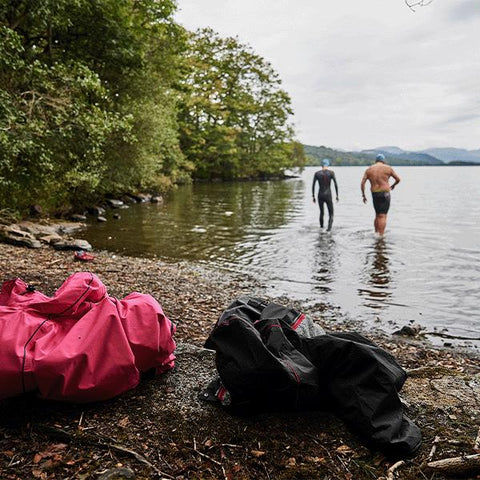 Two men walking into Lake Windemere for a wild swim, leaving their Red Original Pro Change Robe EVO on the shore