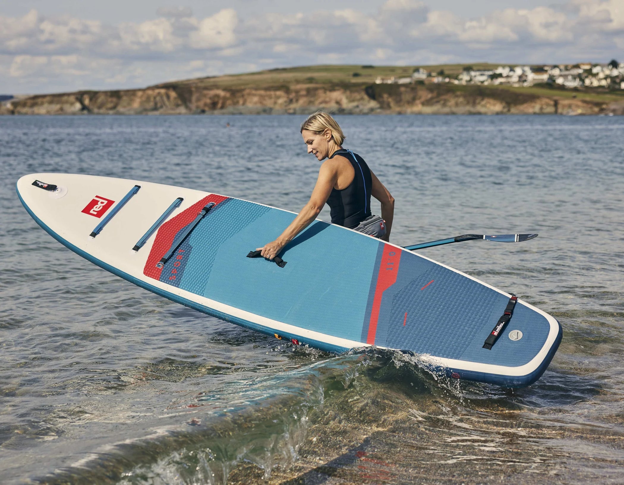 A woman carrying her paddleboard into the sea on a cloudy day