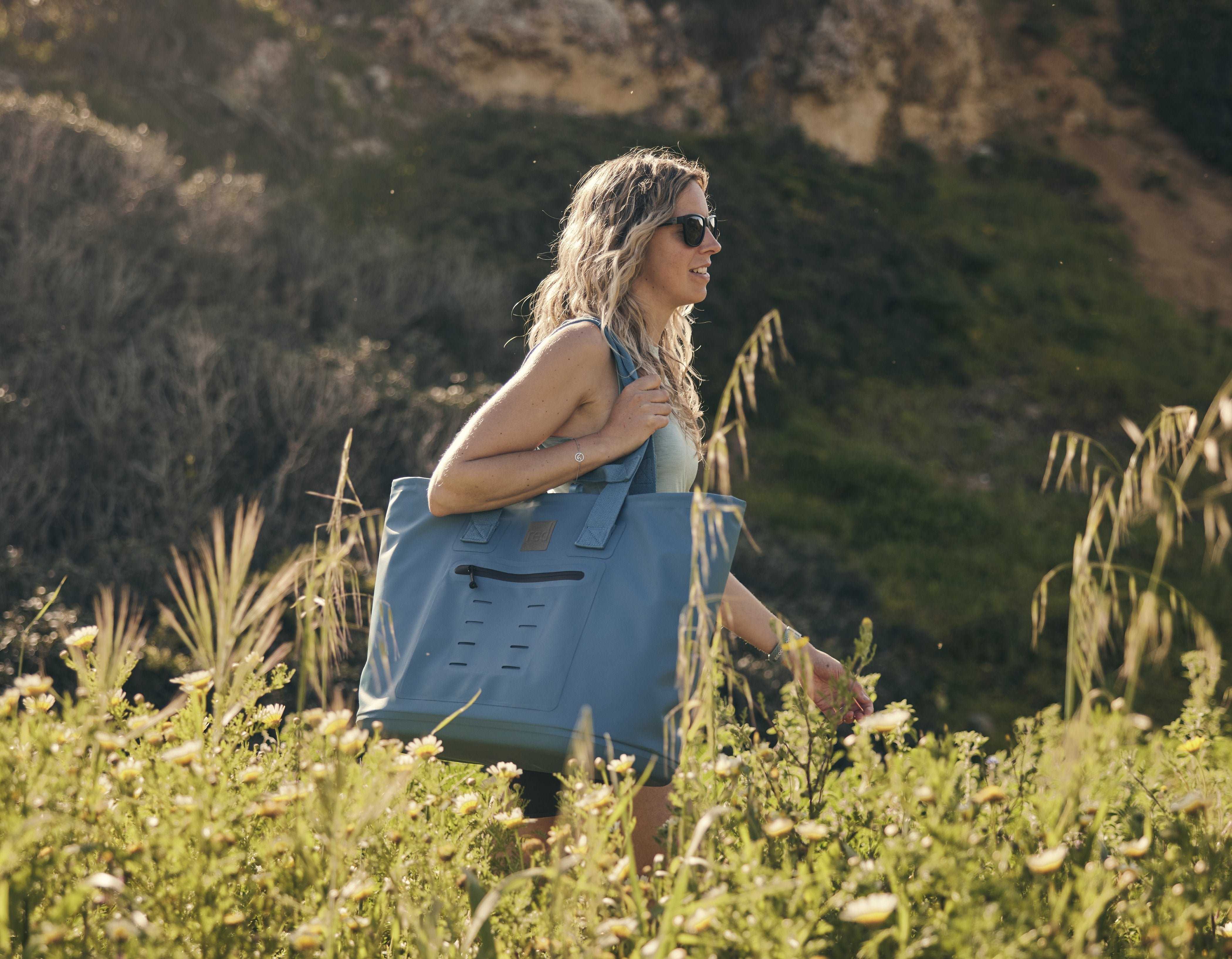 Women walking amongst bushes carrying a Red Storm Blue Waterproof Tote bag. 